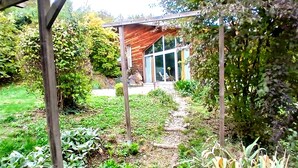 A garden with a wooden pergola, a brick house with large windows, and a stone pathway. - Atypical house in a green setting only 20 minutes from Nice (Contes)
