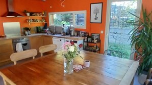 A kitchen with wooden cabinets, a dining table with chairs, a vase with flowers, and a window overlooking a garden. - Atypical house in a green setting only 20 minutes from Nice (Contes)