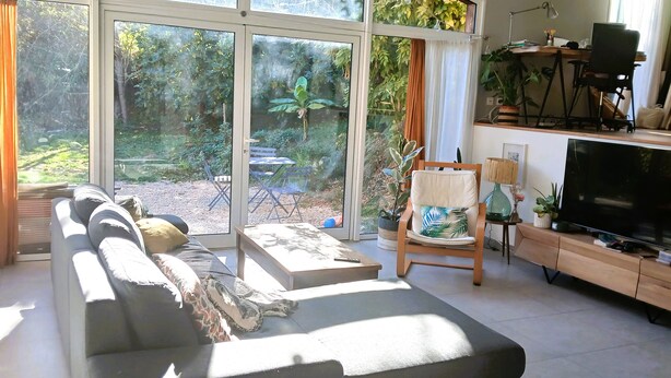 A modern living room with a sofa, a TV, and a dining area with a table and chairs. - Atypical house in a green setting only 20 minutes from Nice (Contes)