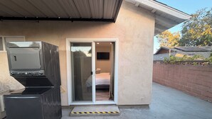 A modern house with a garage door, a sliding glass door leading to a bedroom, and a small outdoor area with a concrete floor.