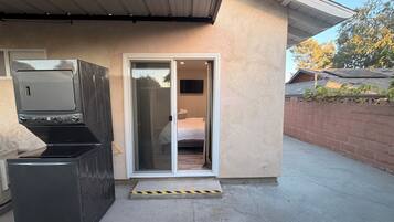 A modern house with a garage door, a sliding glass door leading to a bedroom, and a small outdoor area with a concrete floor.