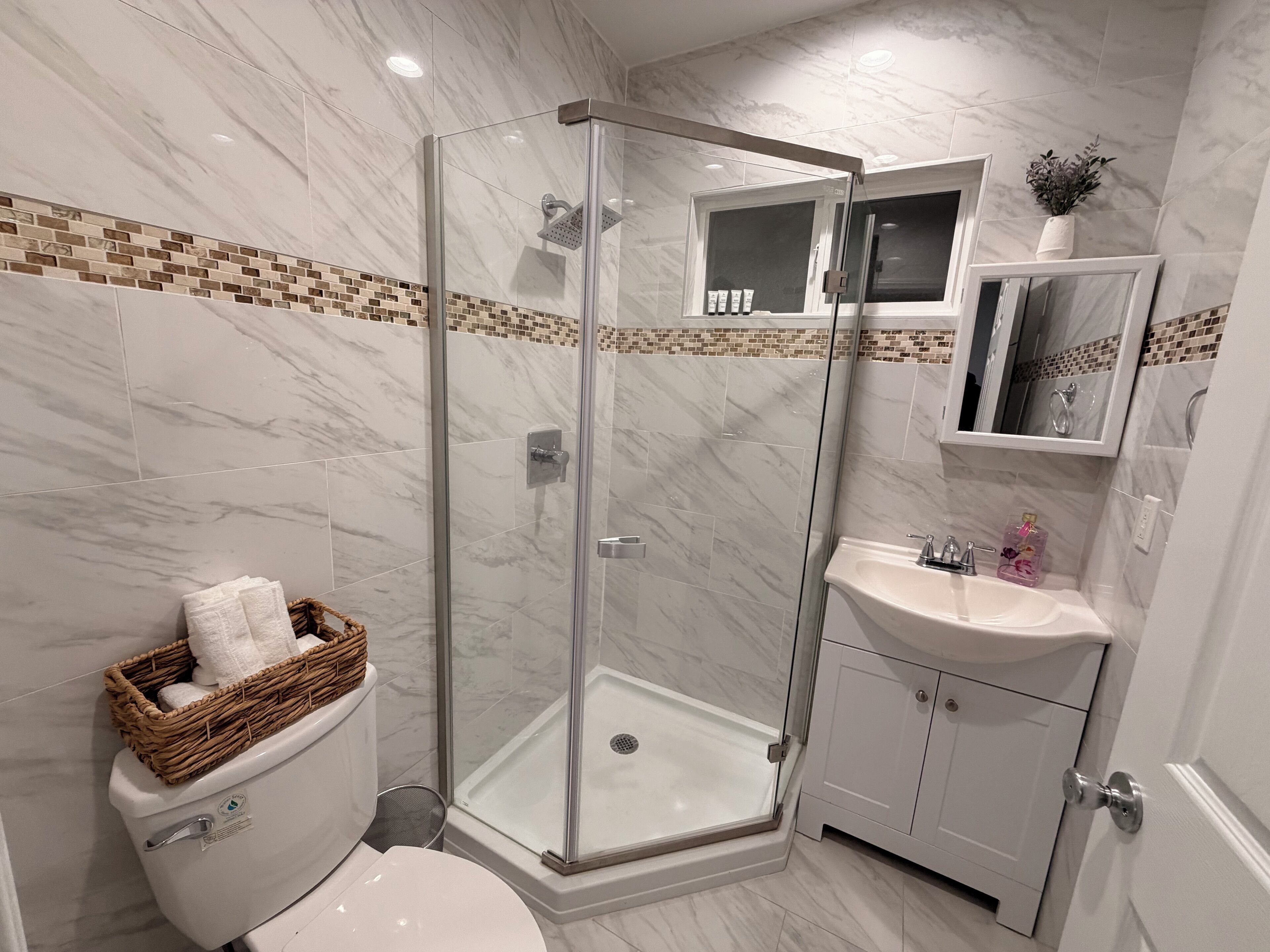 Une salle de bain moderne avec une douche à parois de verre, un lavabo blanc et des toilettes accompagnées d'un panier en osier.