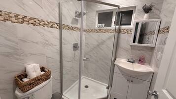 Une salle de bain moderne avec une douche à parois de verre, un lavabo blanc et des toilettes accompagnées d'un panier en osier.