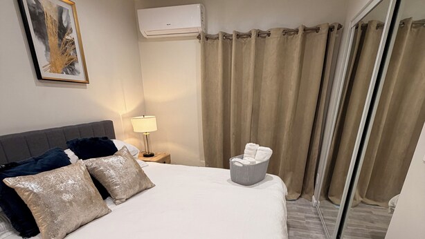 A hotel room with a large bed, a bedside table with a lamp, a wall-mounted air conditioner, and a sliding glass door with curtains.