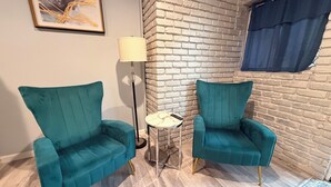 A room with two teal armchairs, a floor lamp, a small round table, and a brick wall.