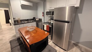 A modern kitchen with stainless steel appliances, a wooden dining table, and grey cabinetry.