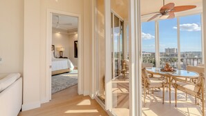 Varanda ampla com mesa e cadeiras de vidro, ventilador de teto e vista para a cidade.