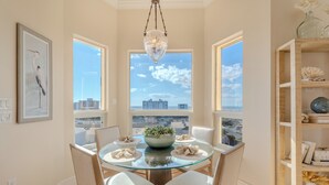 Uma sala de jantar com mesa de vidro, cadeiras brancas, um candelabro e vista para a cidade.