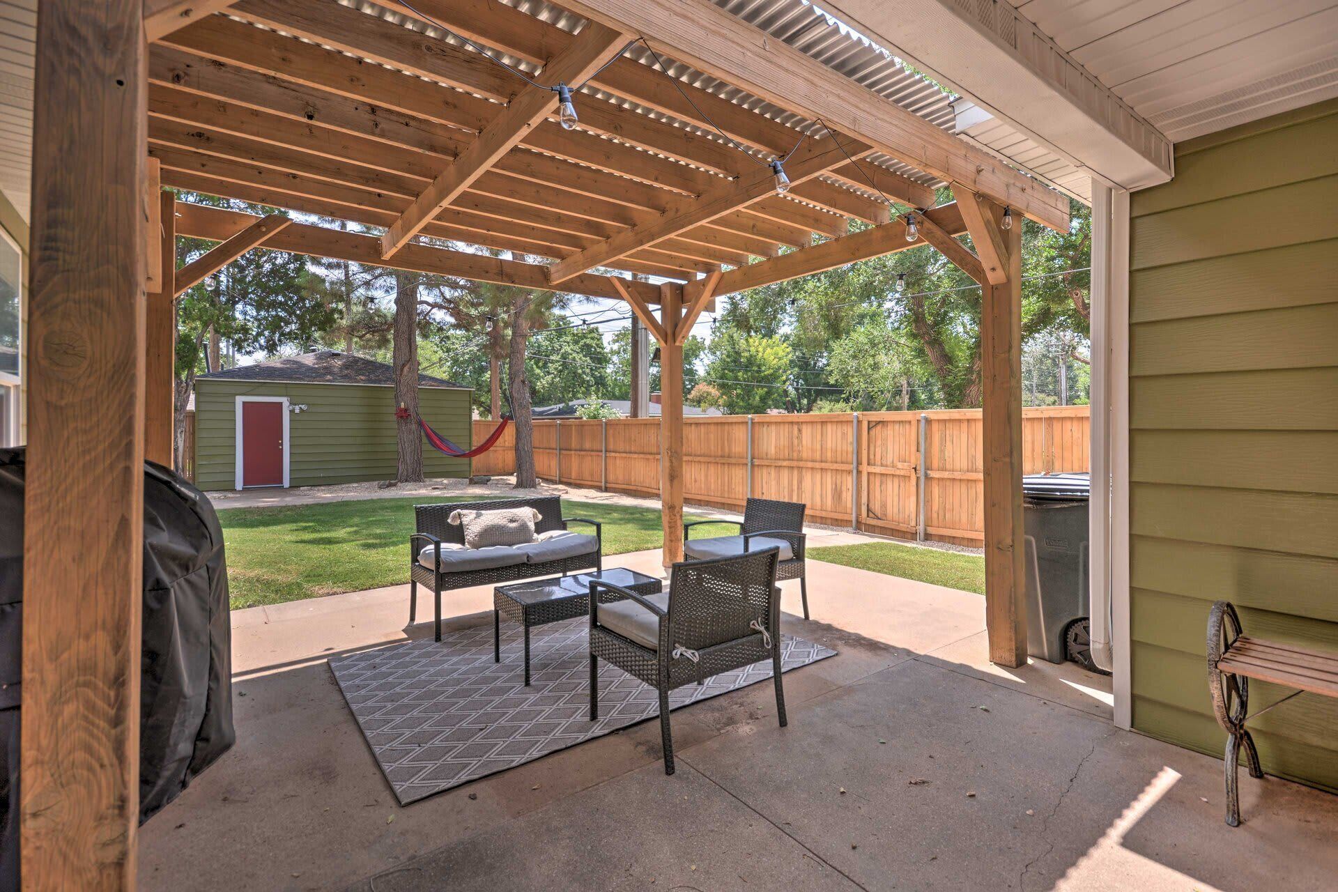 An outdoor patio with a wooden pergola, a grill, and outdoor furniture.