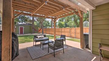 An outdoor patio with a wooden pergola, a grill, and outdoor furniture.