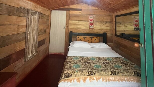 A wooden room with a bed, a door, and a light fixture on the ceiling. - Cabañas el Portal (Santa Rosa de Cabal)