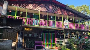 A two-story building with a colorful balcony, a shop on the ground floor, and a garden area with potted plants. - Cabañas el Portal (Santa Rosa de Cabal)