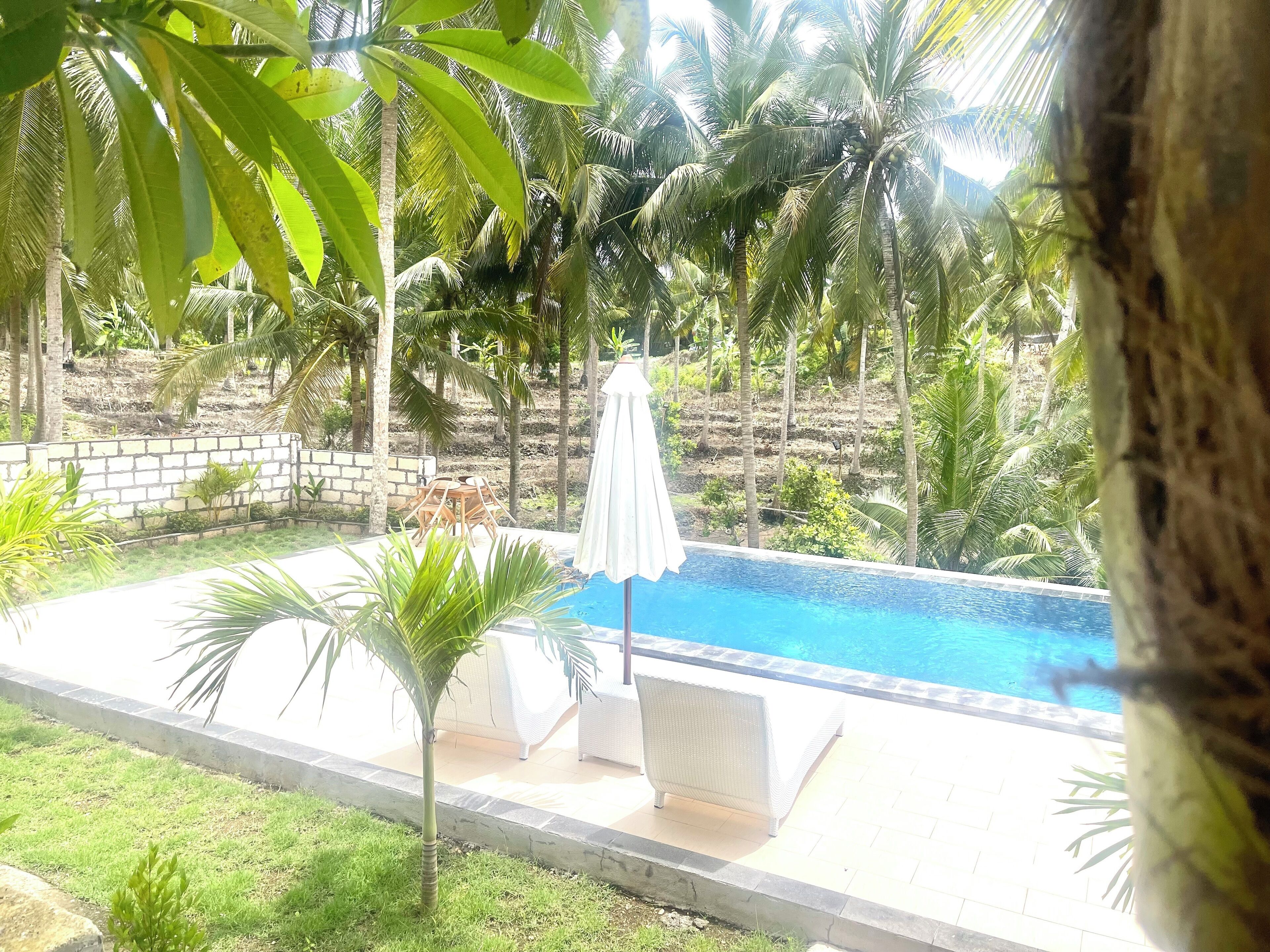 A poolside area with a white umbrella, lounge chairs, and a stone wall.