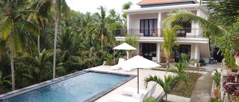 Een buitenzwembad, parasols bij het zwembad en ligstoelen