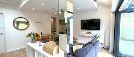 A modern living room with a sofa, a TV, and a dining area with a table and chairs.