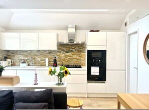 A modern kitchen with white cabinets, a stone backsplash, a Bosch oven, and a sink. - The Secret Garden Fulham (Greater London)