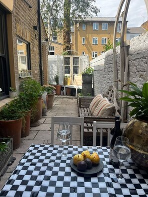 Eine Terrasse im Freien mit kariertem Tischlaken, einer Obstschale und Weingläsern.