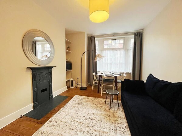 A living room with a fireplace, round mirror, dining table, and black sofa.