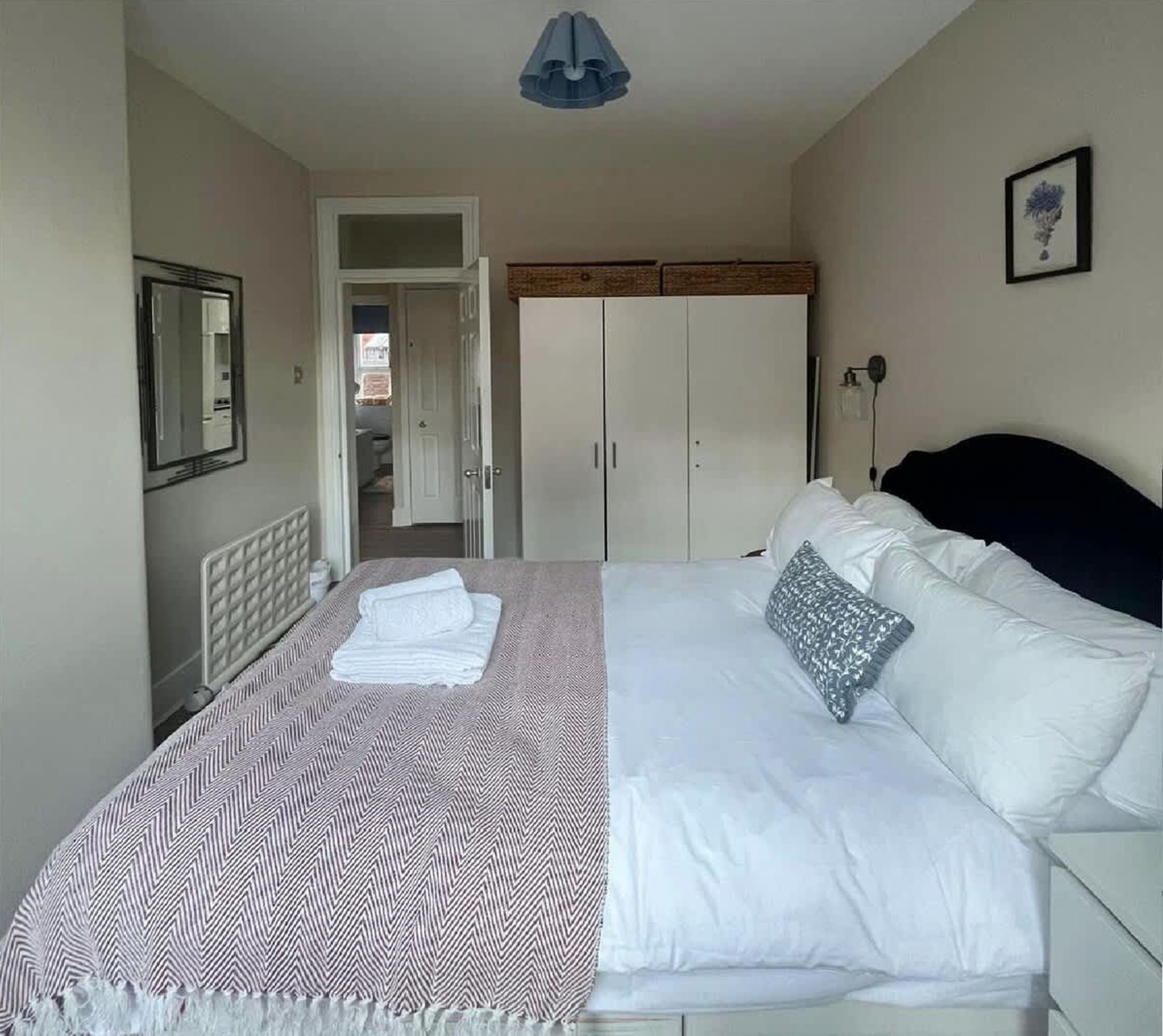 Un dormitorio con cama, armario, espejo y puerta que da a otra habitación.