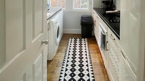 Een kleine keuken met een wasmachine, een koffiezetapparaat en een vloerkleed met een patroon.