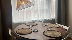 Een ronde eettafel met vier stoelen, een geweven placemat onder elk glas, en één hanglamp erboven.