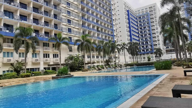 A hotel with multiple balconies, a swimming pool, and palm trees. - Stylish 1-Bedroom at Sea Residences, Pasay — close to SM Mall of Asia! (Pasay City)