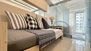 A modern bedroom with a sofa bed, striped pillows, a woven throw, and a vase with flowers. - Stylish 1-Bedroom at Sea Residences, Pasay — close to SM Mall of Asia! (Pasay City)