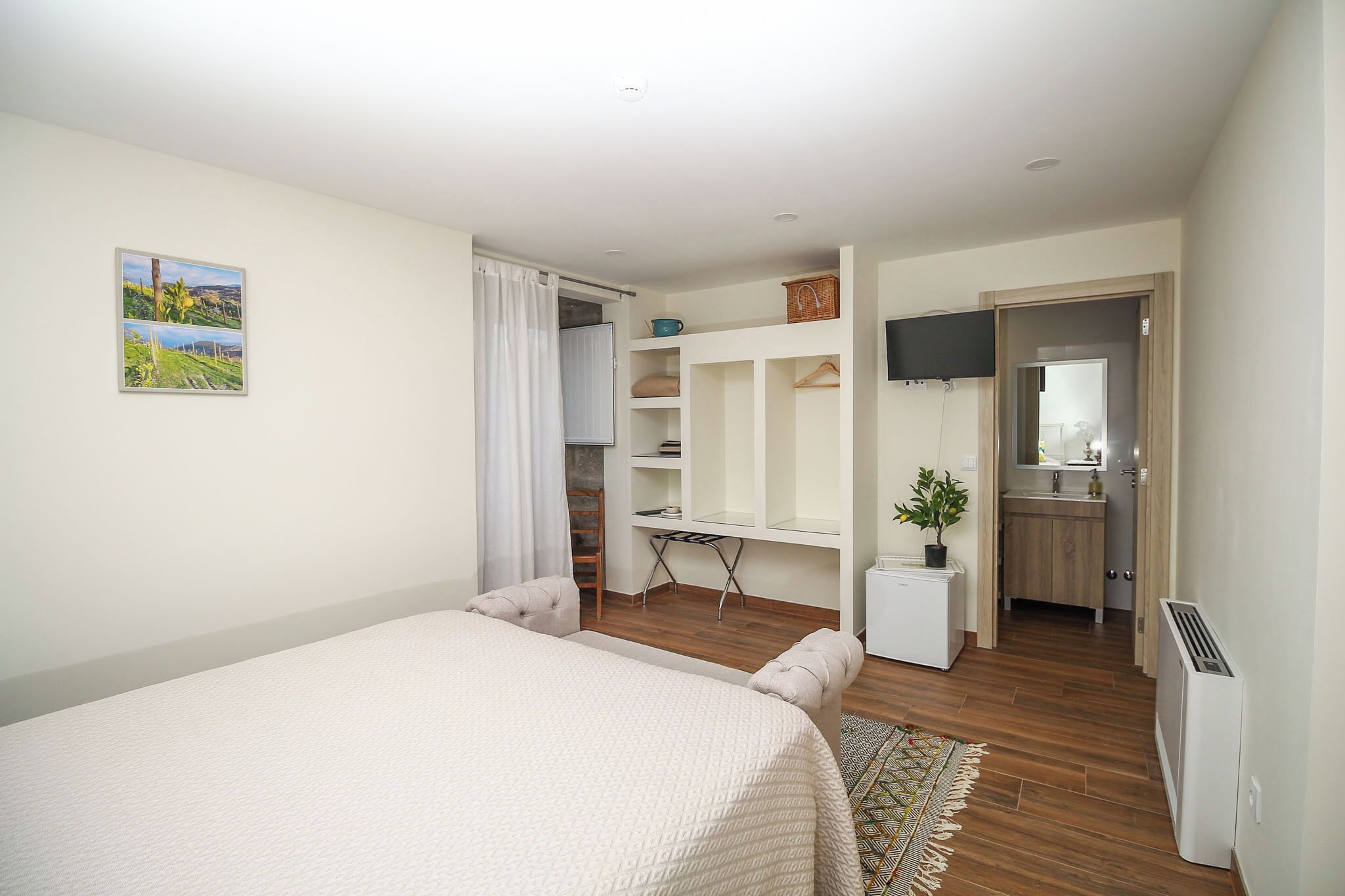 Una habitación con cama, escritorio, televisión y baño a la vista a través de una puerta abierta.
