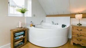 A modern bathroom with a freestanding bathtub, a wooden vanity with drawers, a small bookshelf with books, and a potted plant by the window.