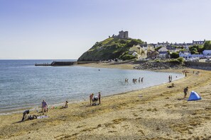 A beach with a castle on a hill, clear skies, and people enjoying the water.