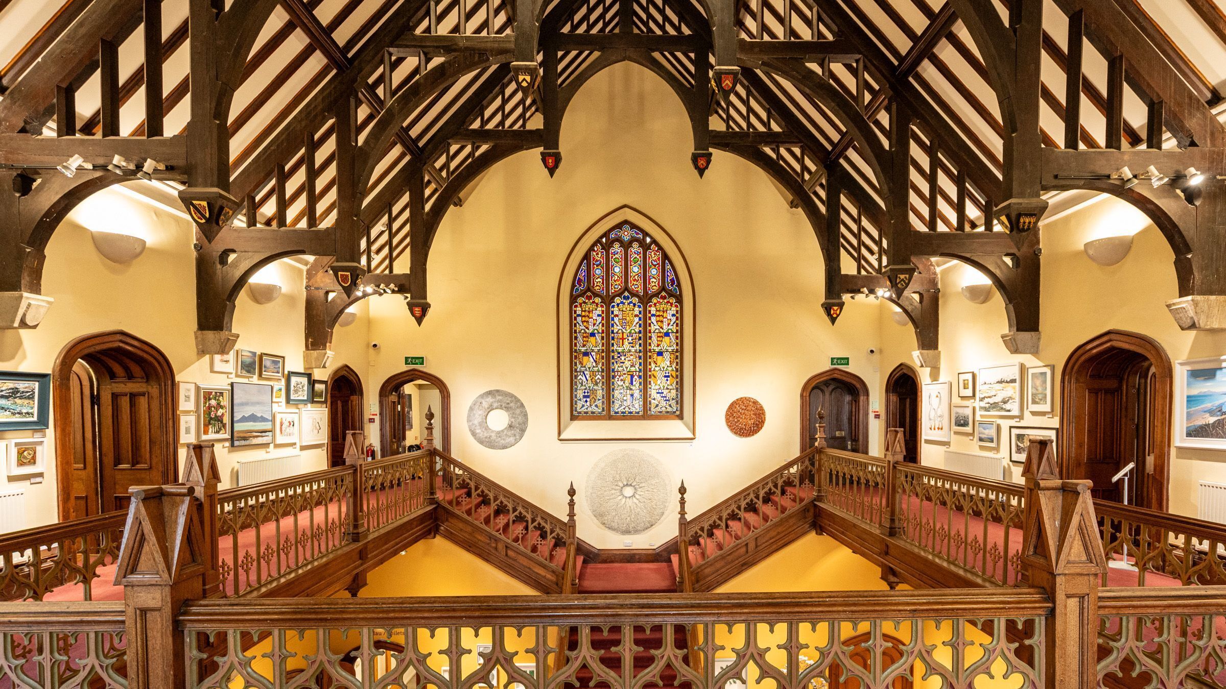 A grand hall with a high ceiling, wooden beams, and a large stained glass window.