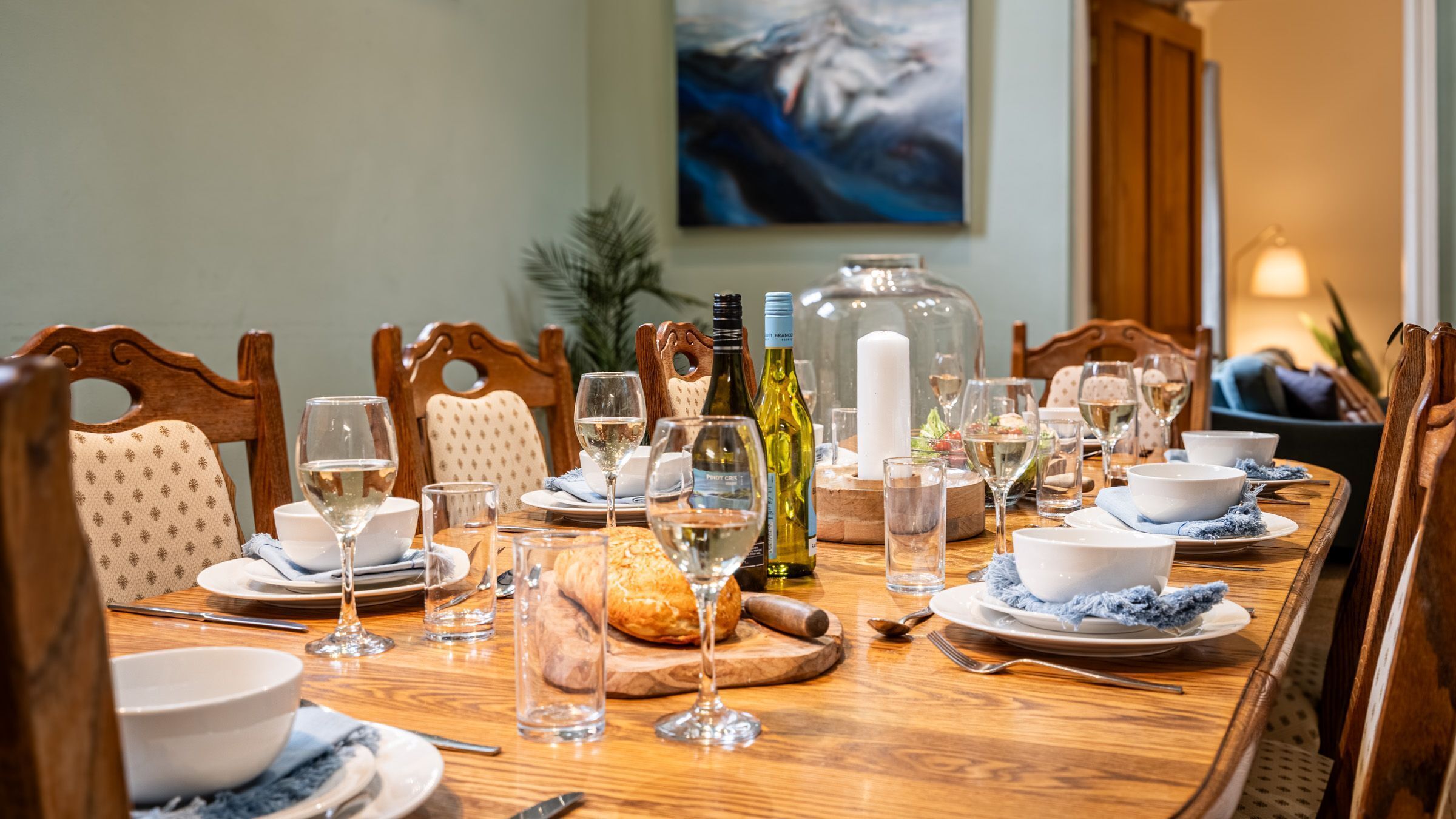 Une table à manger dressée pour un repas, avec des verres à vin, des assiettes et un panier à pain.
