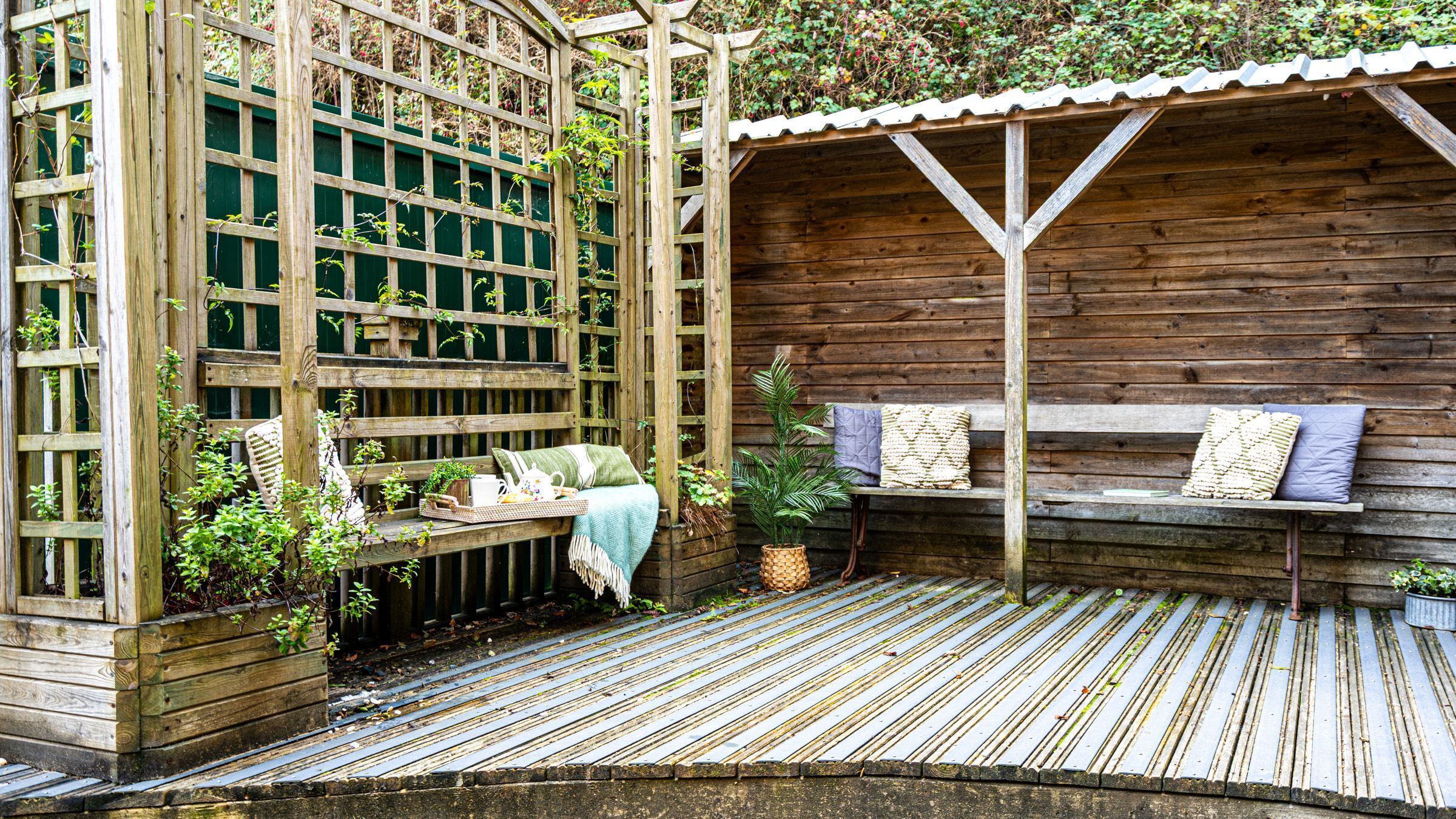 A wooden deck with a bench and a table, surrounded by a wooden fence and plants.