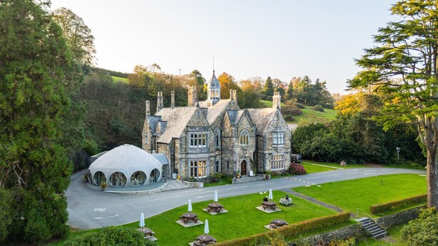 A large stone building with a prominent tower, surrounded by lush greenery and a well-maintained lawn. - Glyn y Weddw - sleeps 8 guests  in 4 bedrooms (Llanbedrog)