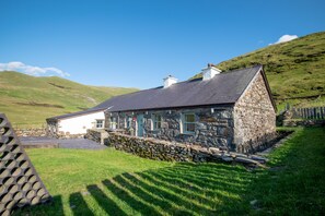 A stone house with a sloped roof, surrounded by a stone wall and a grassy field. - Helfa - sleeps 14 guests  in 3 bedrooms (Llanberis)