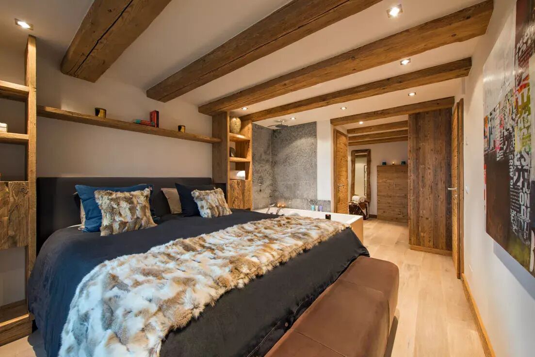 Ein Schlafzimmer mit einem großen Bett, Holzbalken, einer Steinwand und einer Holztür.