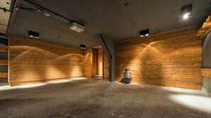 Ein geräumiger Raum mit Holzwandverkleidung und Steinboden, mit großem Kamin aus Stein und eingelassener Beleuchtung.