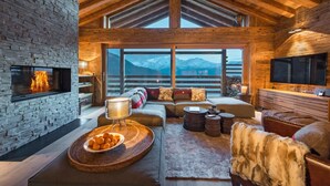 Ein gemütliches Interieur mit Kamin, einer Sofagarnitur, einem Fernseher und Blick auf Berge.