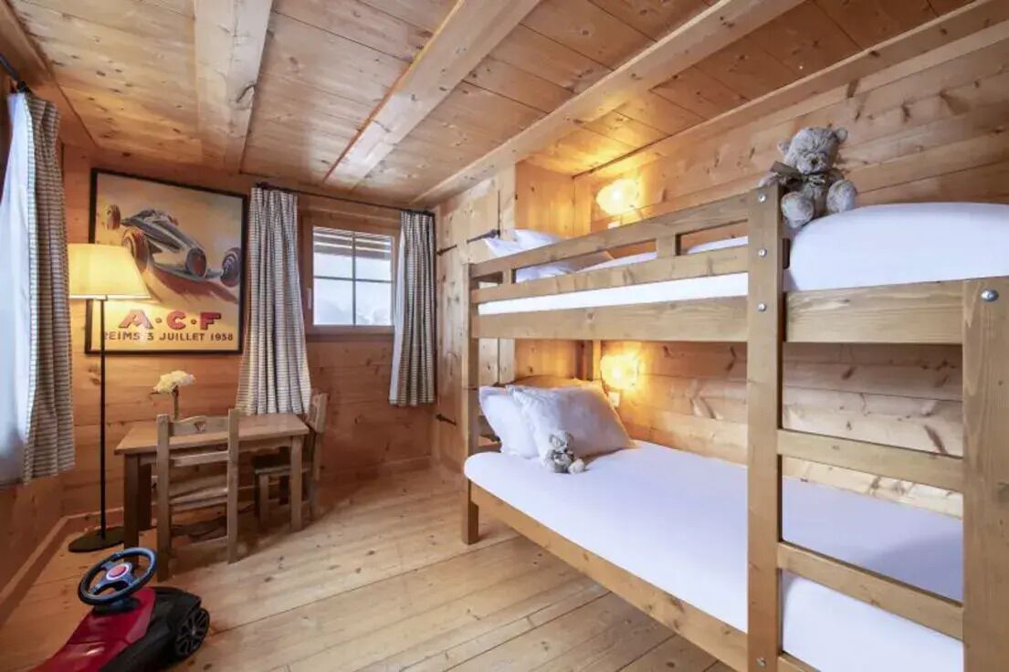 Een houten kamer met stapelbedden, een bureau, een stoel, een lamp en een knuffelbeer.