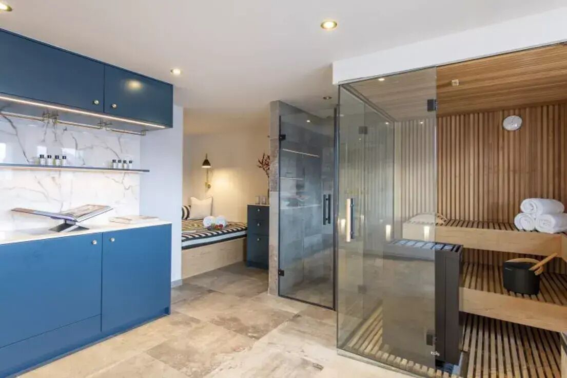 Una cocina moderna con armarios azules, encimera de mármol y zona de sauna con paredes de vidrio.