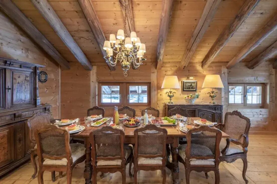 A wooden dining room with a chandelier, wooden chairs, and a table set for a meal.