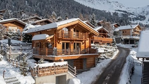 Ein holzähnliches Chalet mit Balkon, umgeben von schneebedeckten Bäumen und Bergen.
