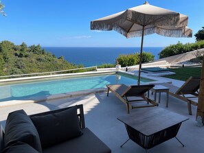 A poolside area with a view of the ocean, lounge chairs, and a table. - Koumaros ApartHotel (Kassandra)