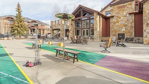 An outdoor patio area with a stone building, seating, and a green sports field. - Grand Timber Lodge Studio Ski in/out (Breckenridge)