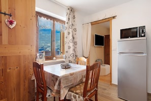 Una cocina con refrigerador, una mesa de comedor con sillas y una ventana con cortinas.