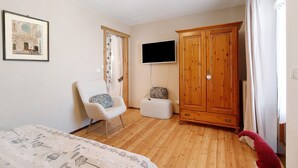 Een slaapkamer met een bed, een stoel, een kledingkast, een televisie en een ingelijst schilderij aan de muur.