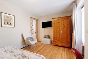 Une chambre à coucher comprenant un lit, une chaise, une armoire, un téléviseur et un tableau encadré accroché au mur.