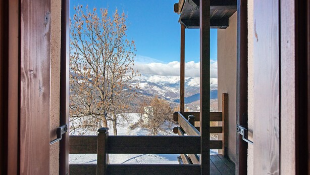Een houten balkon met uitzicht op besneeuwde bergen en een heldere lucht.