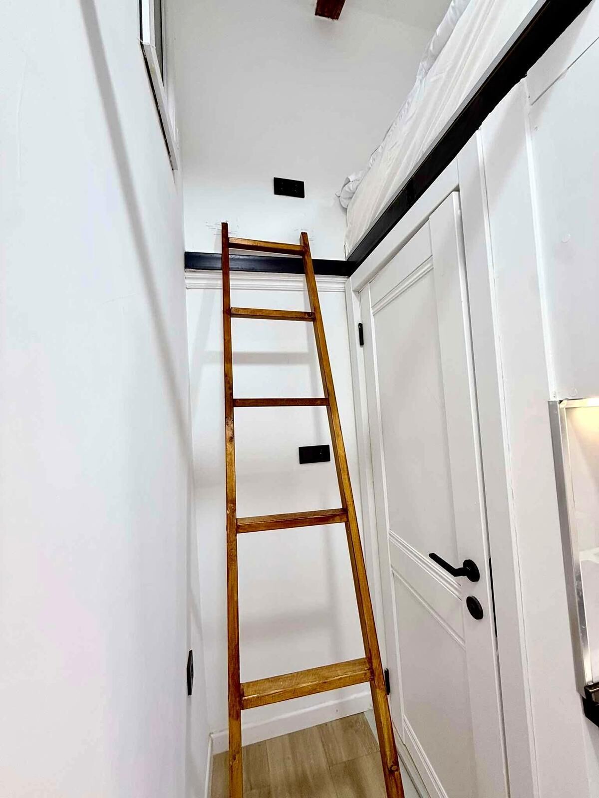 Un couloir étroit, avec une échelle en bois appuyée contre une porte blanche.
