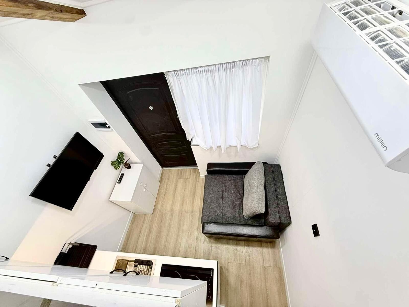 A compact living space with a kitchenette, a dark-colored door, a white curtain, and a white air conditioning unit.